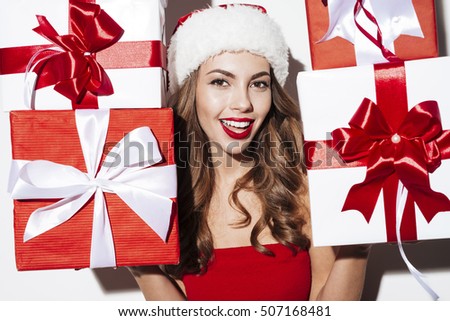 Cheerful cute young woman in santa claus costume holding gift boxes