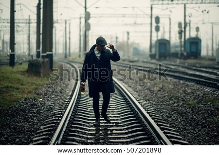 silhouette of stylish gangster man with bottle whiskey walking on railway road. england in 1920s theme. fashionable brutal confident man. atmospheric moments