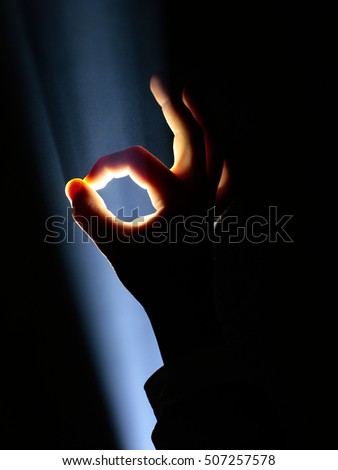 dark silhouette of human male hand with fingers in spotlight or backlight light with okay or ok gesture on black background with dramatic projector shine ray or beam