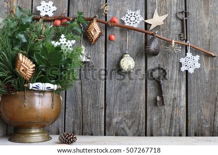 Christmas scene with pine, holly, juniper branches in vintage authentic cooper ashtray, cookie cutters, rustic keys, knitted snowflakes, star, tree of birch bark, red crab apples on branch, glass toy 