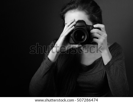 Young female photograph making the photo on dark background holding the camera. Black and white closeup portrait