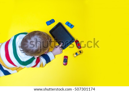 Boy using tablet and laptop while playing with toy cars on a carpet at home. Modern family. Tablet pc hero header image. Boy using digital tablet while lying on yellow floor. 