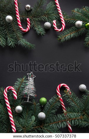 Christmas or New Year decoration background. Fir tree branches, spruce, candy, colorful balls on black background with copy space. Top view.
