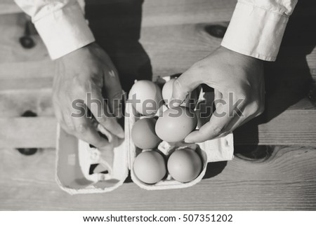 Black and white image top view closeup of person hand taking an egg out of the carton box on table background. Counting or selecting precedure