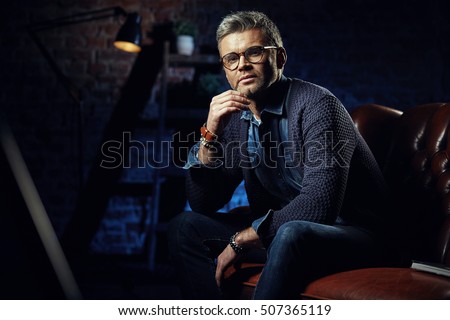 Portrait of handsome stylish man with gray hair sitting in studio