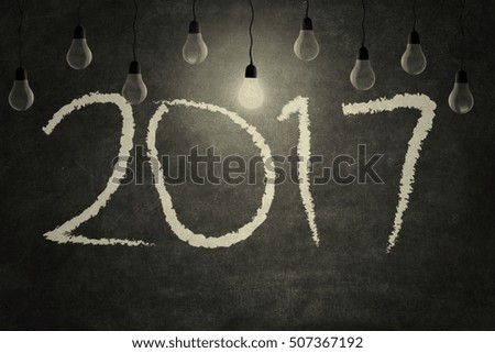 Bright light bulb flashing on the number 2017 on blackboard. Isolated on bokeh background