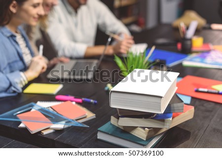 Preparing to exams. Close up photo of books lying on table with students sitting at desk and learning in background