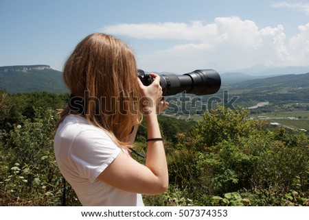Young woman photographer taking landscape photo with professional camera with telephoto lens