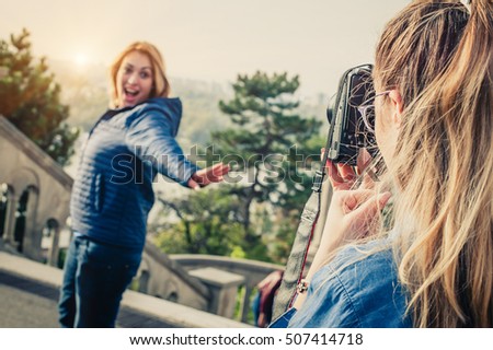 Shot of a girl photographer taking a picture of a her friend with dslr camera. Outdoors photo shoot