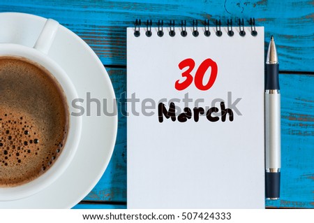 March 30th. Day 30 of month, calendar on blue wooden table background with morning coffee cup. Spring time, Top view