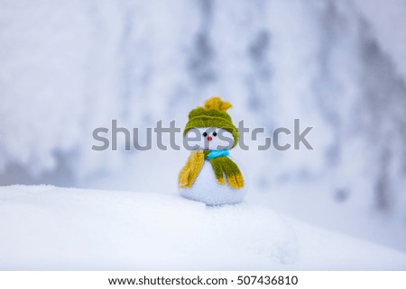On the white fluffy textured snow alone snowman the friend is standing in nice hat and scarf with red nose.