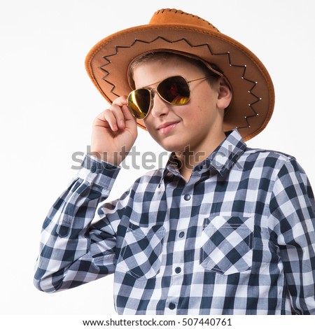 Emotional blond boy in a plaid shirt, sunglasses and a cowboy hat on a white background