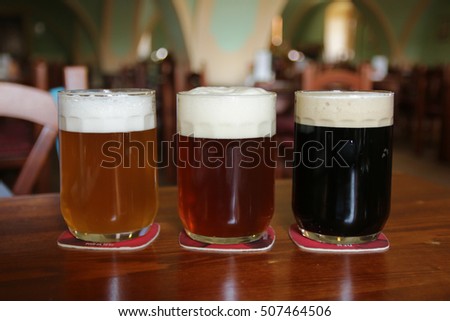 three glasses with different beers on wooden table in restaurant