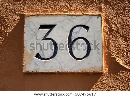 Engraved building number (36) made with marble on plastered wall in Rome.