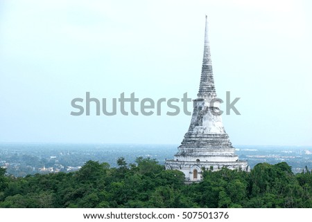 the white ruined and abandoned buddhist stupa or Pranakorn Kiri pagoda shrine standing among the forest on the Khao Wang mountain with urban-scape background at Petchaburi, Thailand.