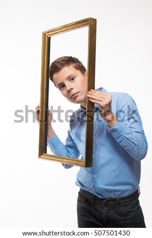 Emotional boy brunette in a blue shirt with a picture frame in the hands on a white background