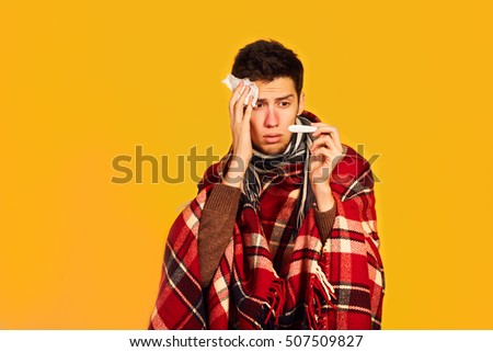 boy looks at the thermometer a surprised look.picture from a young man with handkerchief.  I am sick. plaid wrapped himself. studio shot. 