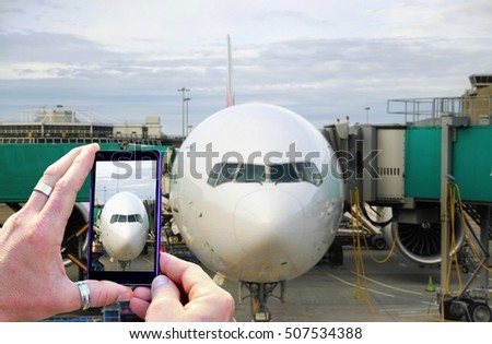 View over the mobile phone display during taking a picture of big airplane at airport. Holding the mobile phone in hands and taking a photo of an airplane. Focused on mobile phone screen.