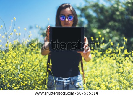 Girl traveler with sunglasses using gadget on sun flare and yellow flowers background, mockup of blank empty screen copy space for text. Hipster holding in hands tablet computer or cell camera