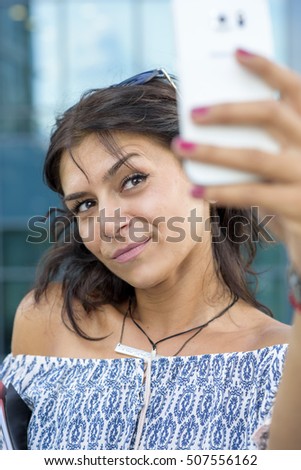 Young casual businesswoman taking a photo of herself, a selfie, outside her workplace