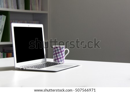 Laptop and a cup on white table with bookshelves in background