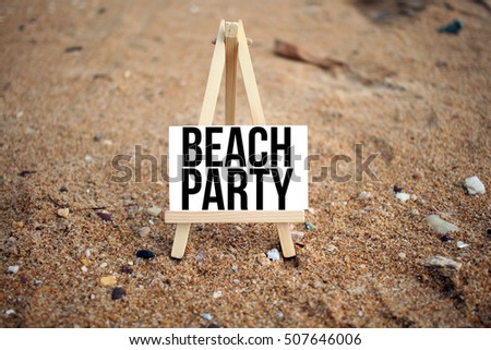 conceptual image on a sandy beach with word BEACH PARTY on white canvas frame with wooden tripod stand. Selected focus - depth of field of sand at the beach