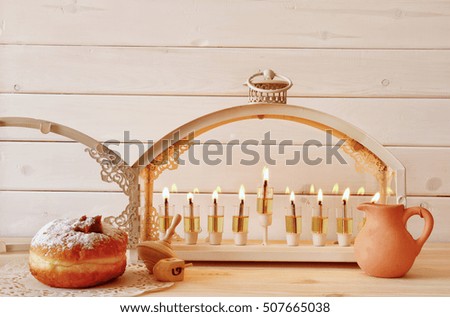 Selective focus image of jewish holiday Hanukkah with menorah (traditional Candelabra), donuts and wooden dreidel (spinning top)