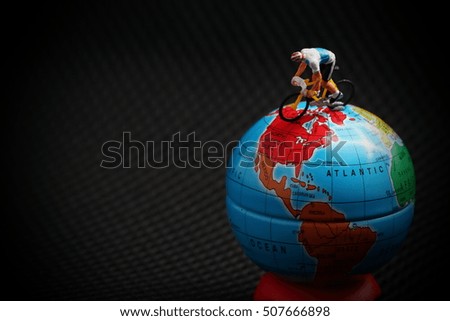 Miniature figure plastic model of cyclist on racing bicycle put on the globe model.  