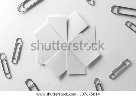 Blank business cards fan stack with scattered clips at white textured paper background.