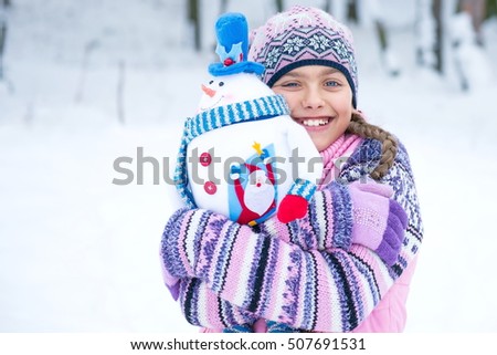 Happy girl with a gift for Christmas. Happy Winter Girl With Snowman Doll. Beautiful girl with a gift Christmas Toy Outdoor. Bright picture of teenage winter holidays. Concept winter emotions