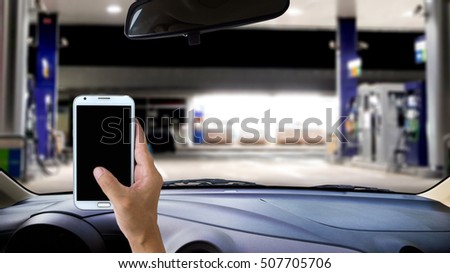 Man using a mobile phone while driving, blur image of gas station as background.