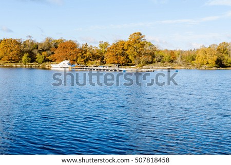 Fall in the coastline. Two boats moored along a pier with colorful landscape in background. Jarnavik in southern Sweden. Royalty-Free Stock Photo #507818458