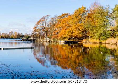 Windless and calm sea in fall with colorful trees and fine weather. Jarnavik just outside Ronneby in Sweden. Royalty-Free Stock Photo #507818470
