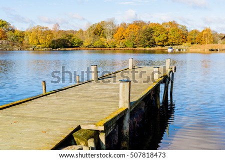 Wooden pier stretching out into the sea towards a small motorboat in the distance in fall. Jarnavik just outside Ronneby in Sweden. Royalty-Free Stock Photo #507818473
