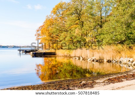 Windless and calm sea in fall with colorful trees and fine weather. Jarnavik just outside Ronneby in Sweden. Royalty-Free Stock Photo #507818485