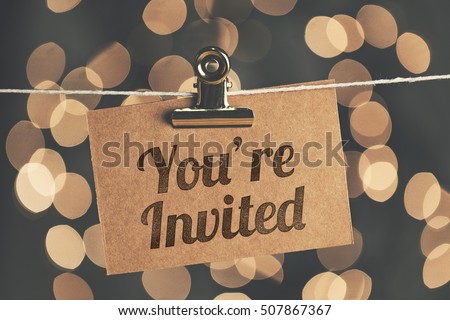 You're invited sign pegged to a string with blurred bokeh lights in the background