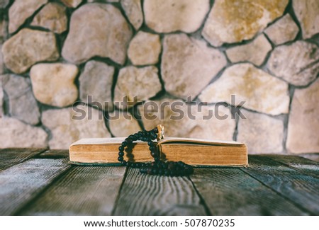 prayer beads with a cross on an open old book on old wooden table on a background of stone walls. selective focus, toning photo. with space for your text