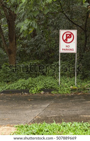 No parking sign. White sign 'no parking' standing near asphalt road surrounded with green grass and trees. 