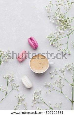 Morning cup of coffee, cake macaron and flower on light background from above. Beautiful breakfast. Flat lay style.