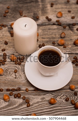 Small white cup of coffee, hazelnuts, cocoa beans, candle on wooden background