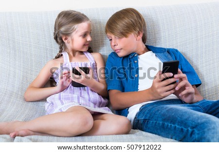 Smiling little girl and teenage boy burying in mobile phones sitting on the sofa
 Royalty-Free Stock Photo #507912022