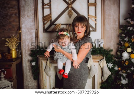 tender photo of beautiful mother  posing with her cute little baby girl beside Christmas tree in cozy home