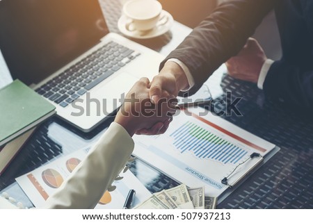 Businessman handshaking for business cooperation, Chart documents showing income structure and a laptop, along with a large number of banknotes placed on the table for signing commercial contracts. Royalty-Free Stock Photo #507937213