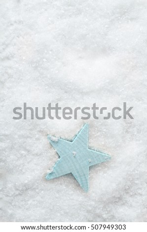 Christmas background image. Overhead shot of a pale blue wooden star on artificial white snow with copy space above.