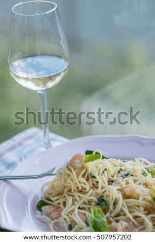 spaghetti with shrimp and spinach on a pink plate with a glass of white wine