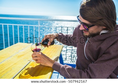 Man pouring wine on a ship or ferry boat at sea landscape. Red alcohol in glass. Tourist in sunglass at the sea.