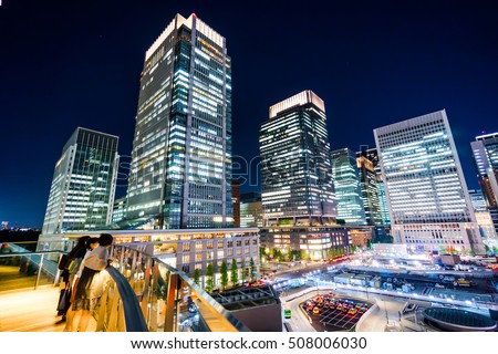 Asian Business concept for real estate and corporate construction - panoramic modern cityscape building bird eye aerial night view of Tokyo Station and young girls under neon blue sky in Tokyo, Japan