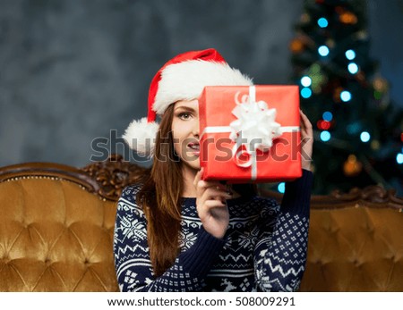 Close-up of beautiful woman with a Christmas present. Young girl celebrating xmas. Tree on a background. Holidays, winter and celebration concept.