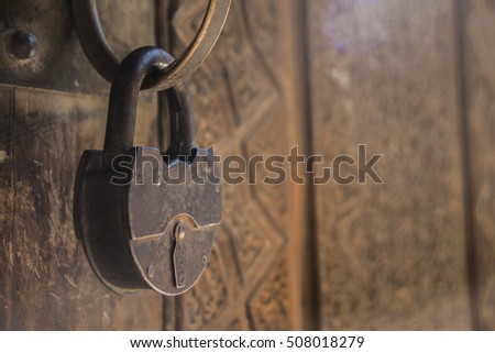Architectural vintage background - old rusty metal padlock hanging on the wooden textured door. Focus at the padlock. Retro tones processing.