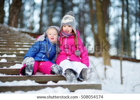Two funny adorable little sisters having fun together in beautiful winter park